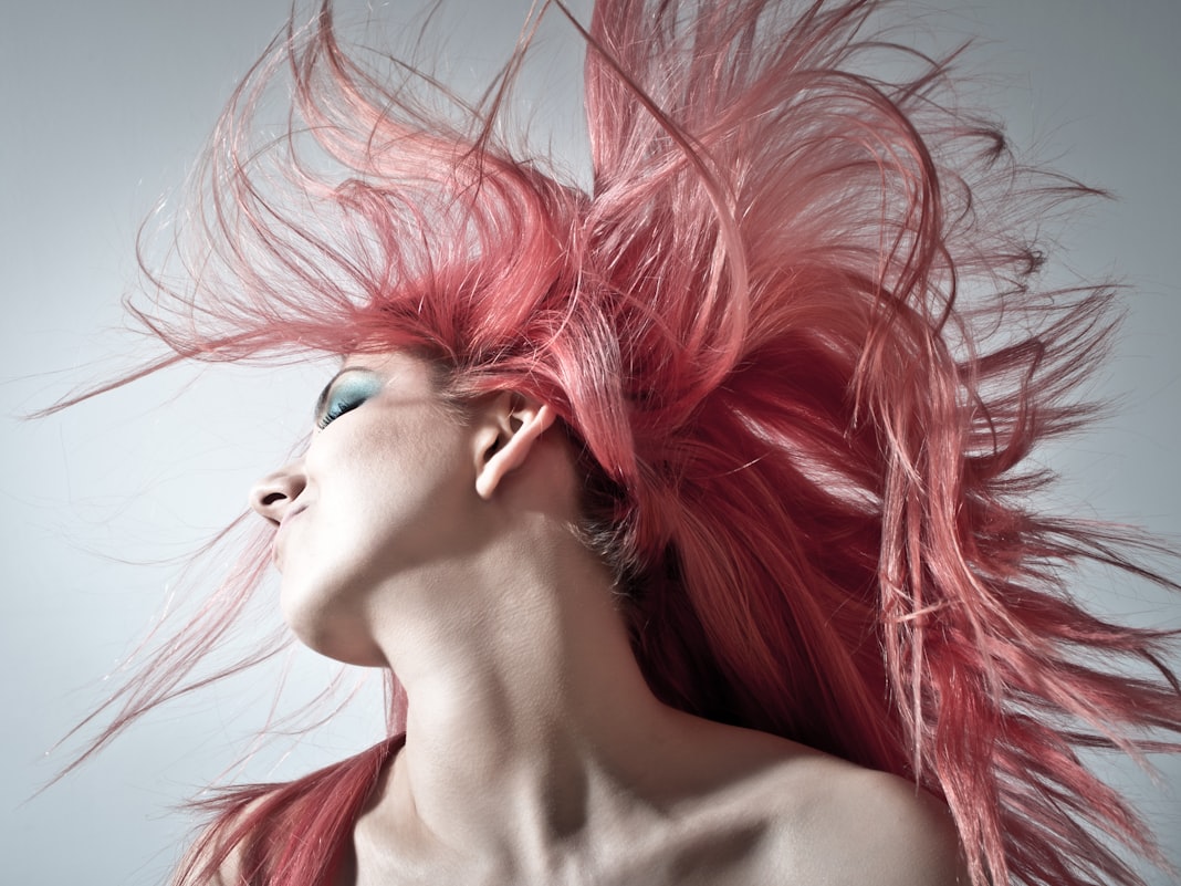 Long pink-toned hair caught mid-movement against a pale background